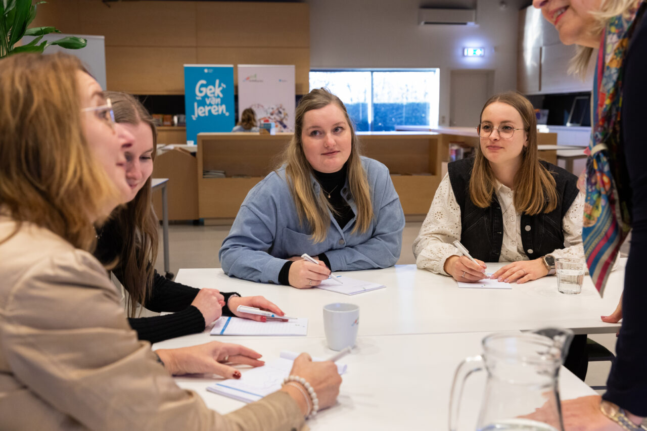 Een groep vrouwelijke docenten luistert aandachtig naar elkaar tijdens een training, waarbij ze actief met elkaar in gesprek zijn