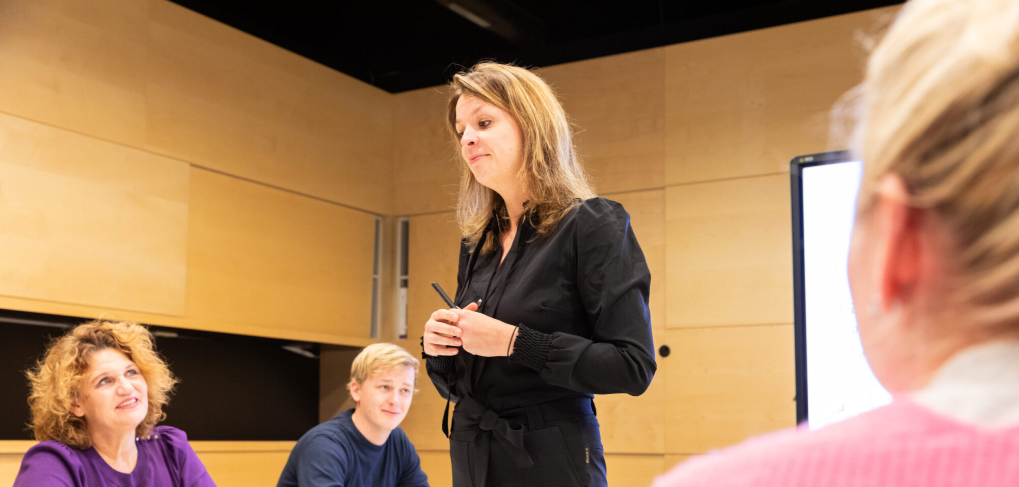 Een vrouwelijke trainer legt een onderwerp uit, terwijl een groep docenten aandachtig luistert tijdens een training.